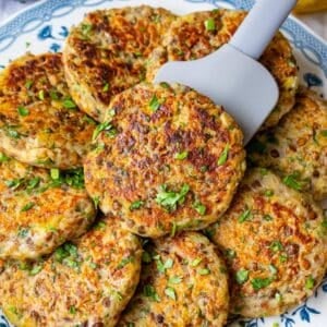 Golden brown lentil potato patties cooked on a skillet with olive oil and served on a plate with parsley.