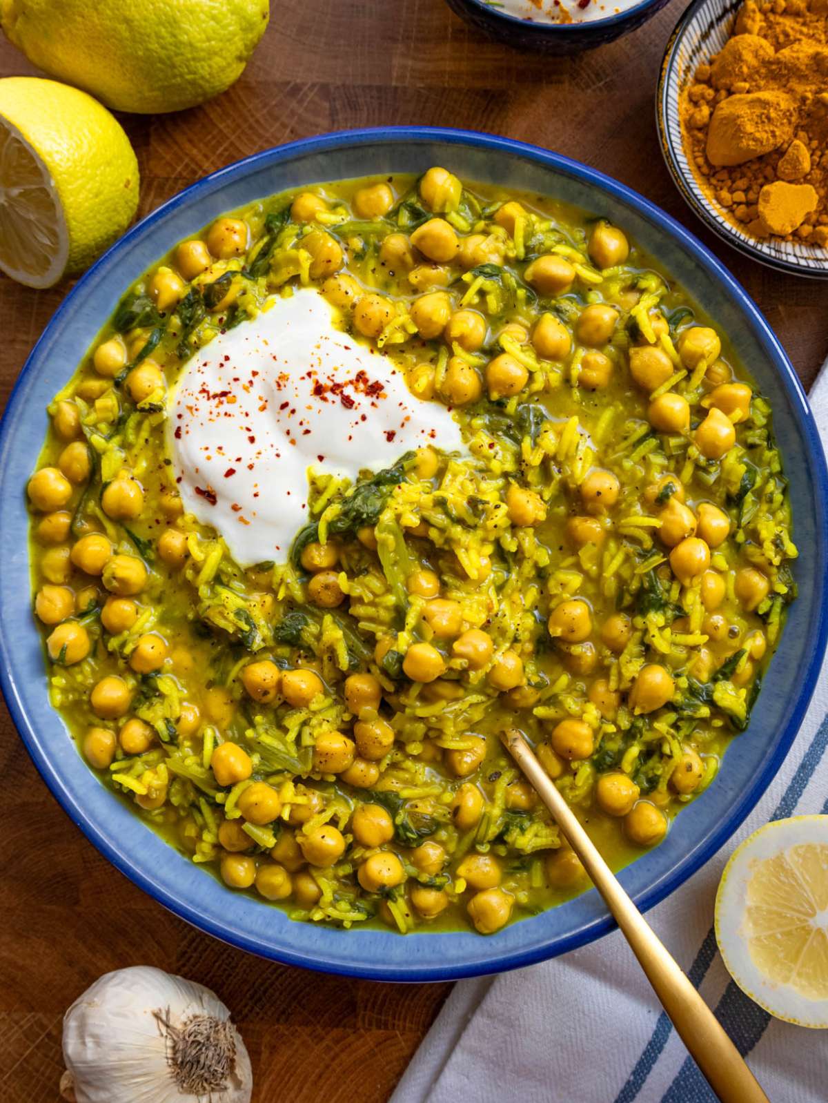 Golden turmeric rice with chickpeas and spinach served in a bowl with lemon wedge squeezed on top.