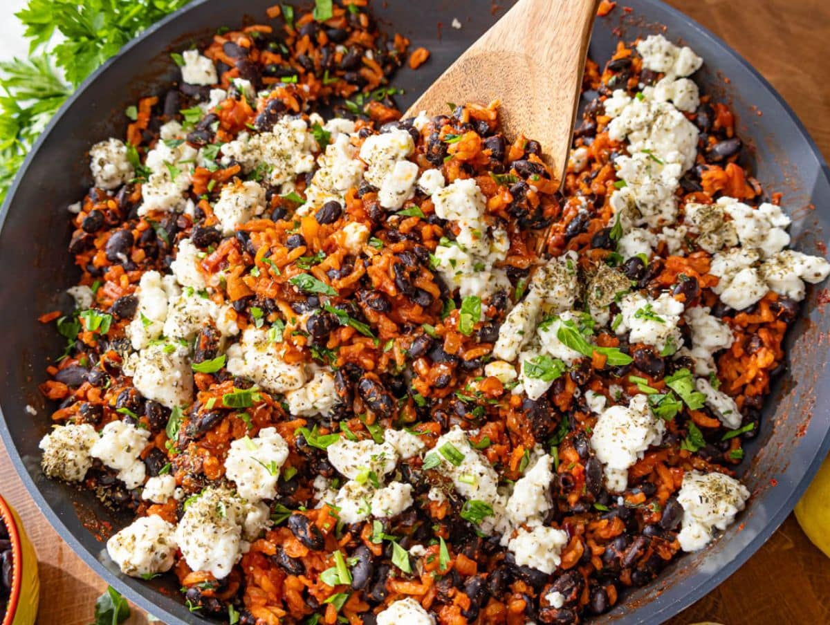 Healthy black beans and rice in skillet showcasing vibrant colors and creamy marinated feta.