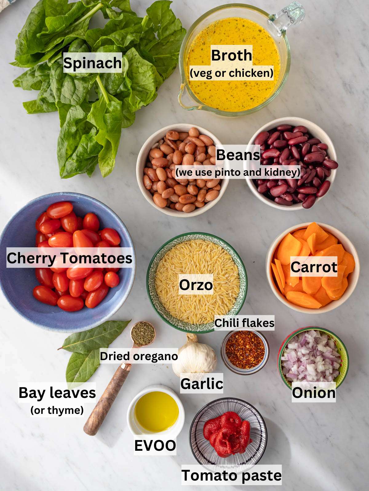 Ingredients for orzo and beans arranged on marble table with fresh veggies and canned beans.
