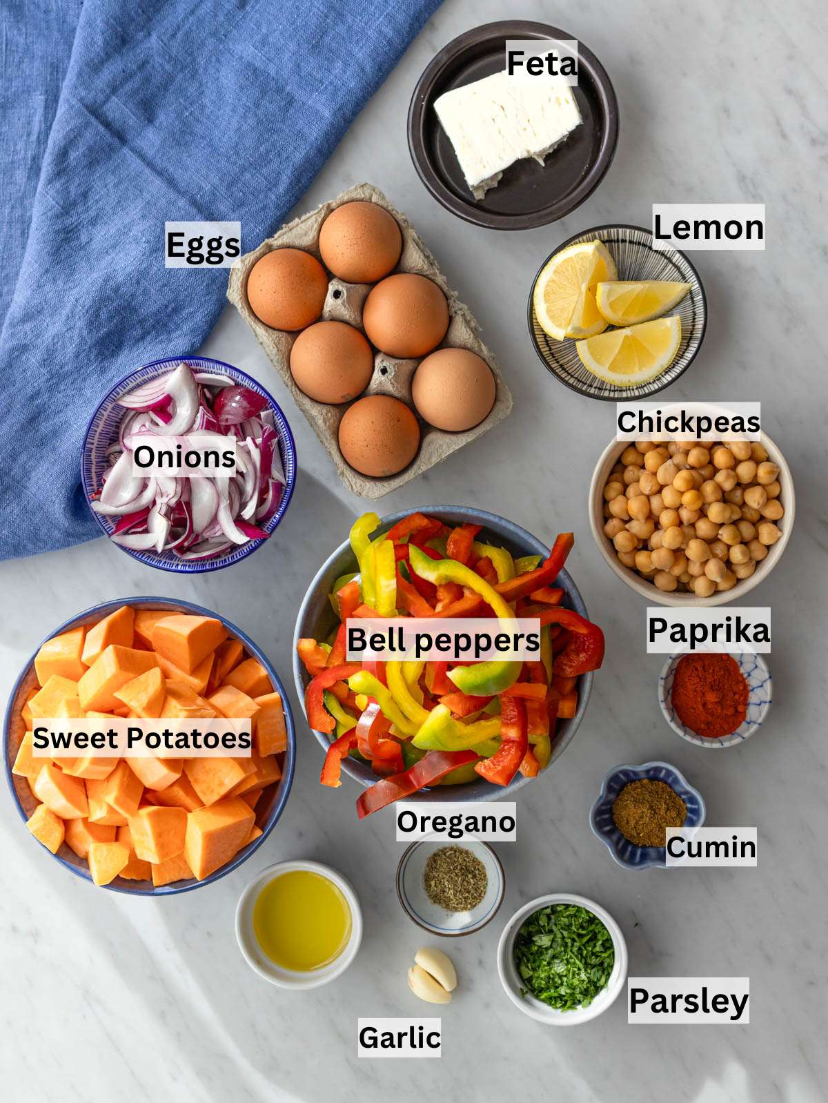 Ingredients laid out for sheet pan eggs and veggies sweet potatoes chickpeas peppers and spices.