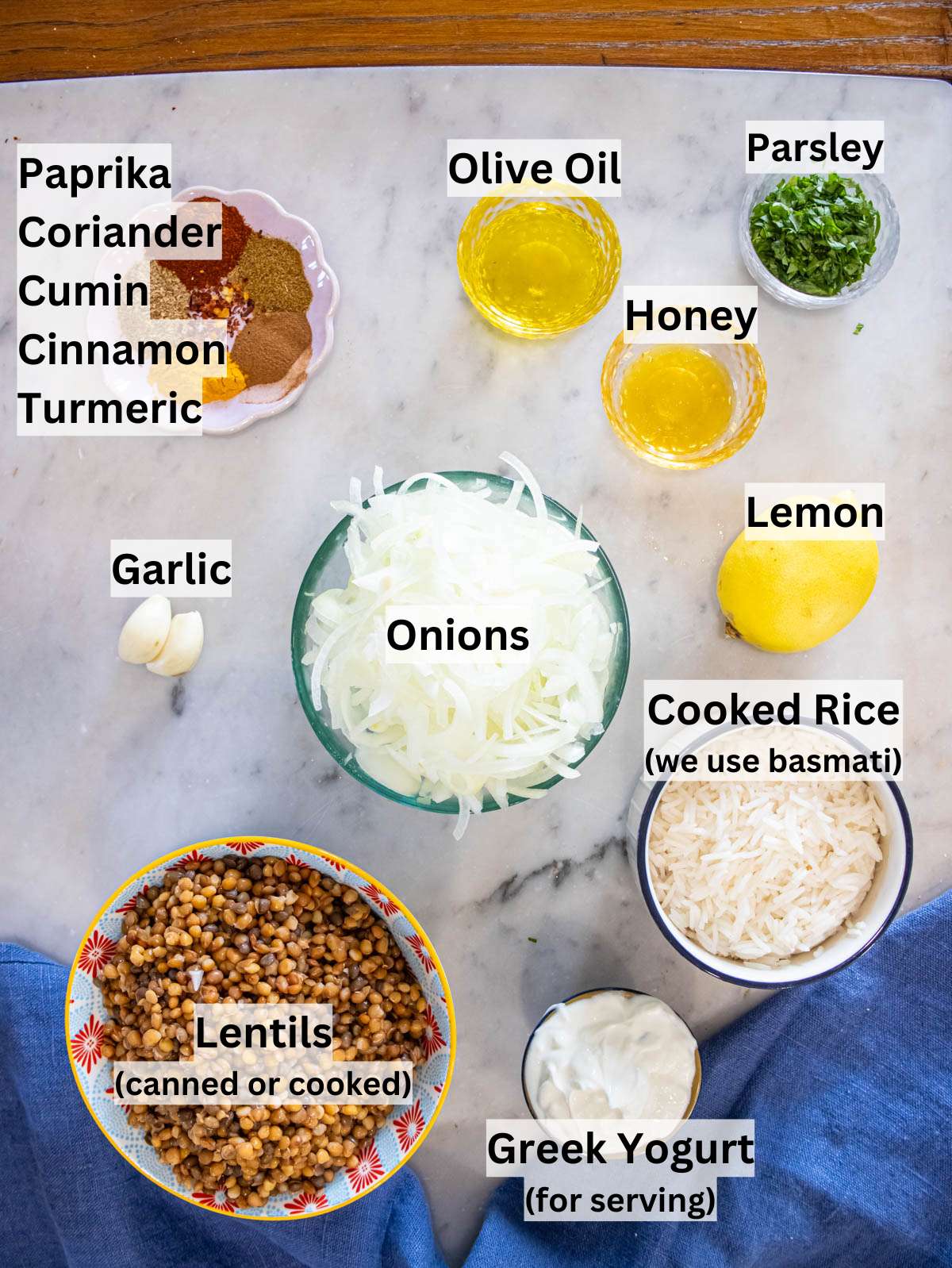 Ingredients picture with canned lentils, rice, onions, spices, olive oil, and lemon arranged on marble table.