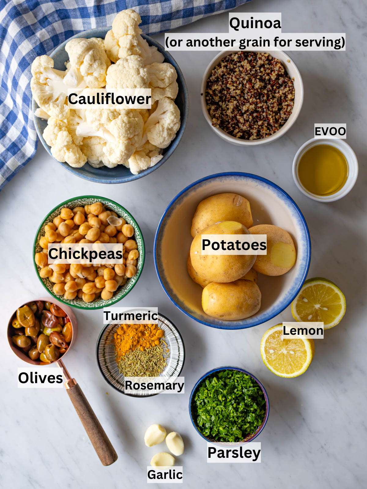 Ingredients shot cauliflower potatoes chickpeas olives spices and lemon arranged on table.