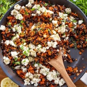 One pan Mediterranean black beans and rice served with feta parsley and lemon on wooden table.
