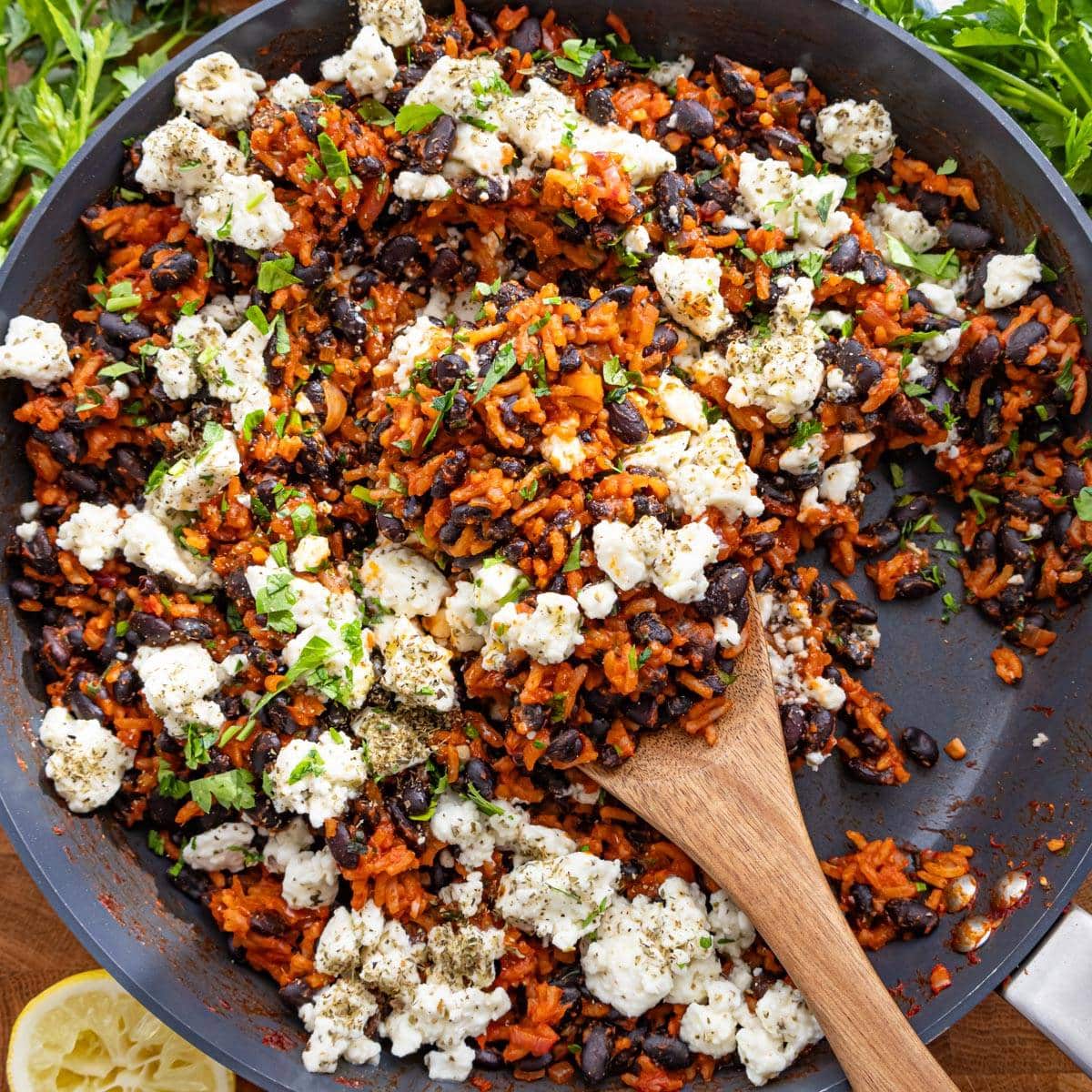 One pan Mediterranean black beans and rice served with feta parsley and lemon on wooden table.
