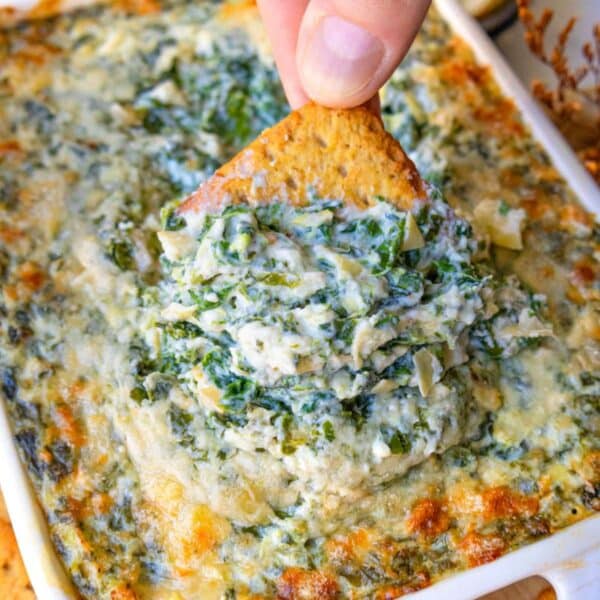 Picture of creamy spinach artichoke dip with cracker dipped showing rich texture.