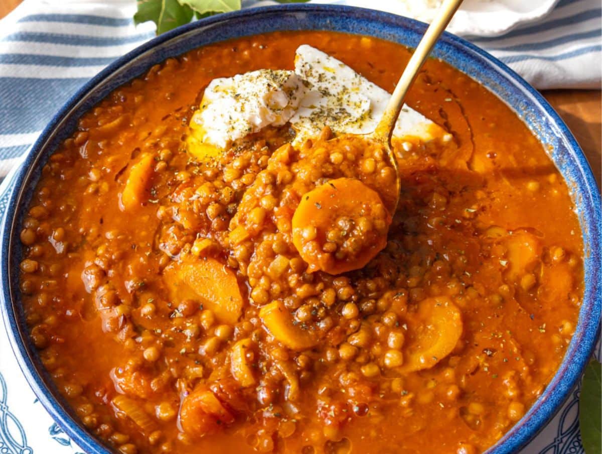 Rustic bowl of Greek lentil soup with olive oil drizzle chunks of feta and oregano on top.