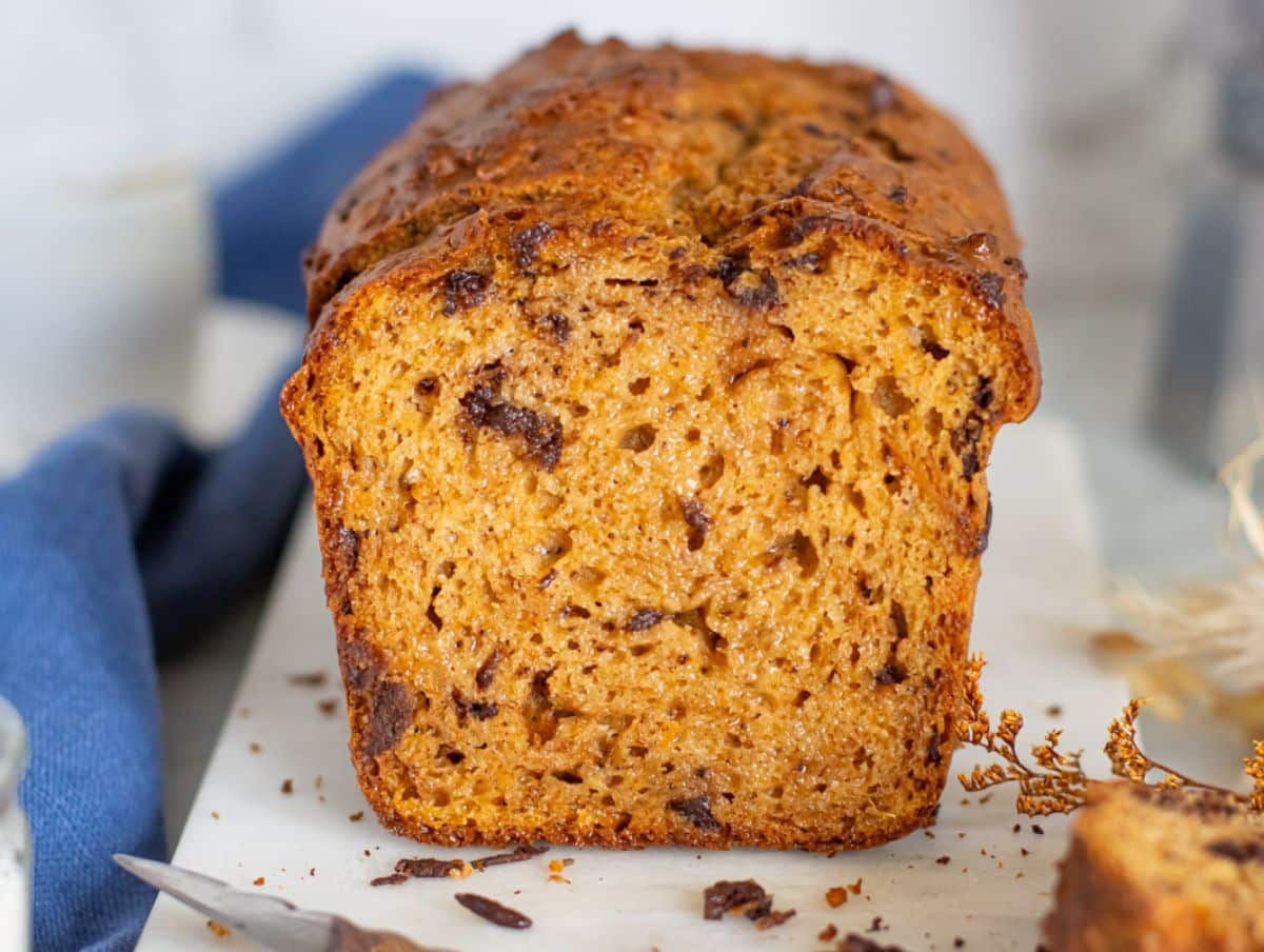 Sliced sweet potato bread loaf on cutting board surrounded by chocolate chunks and a blue cloth.