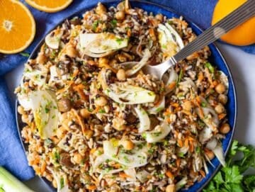 Step 4 Mediterranean diet friendly wild rice salad served on a blue platter with a silver spoon.