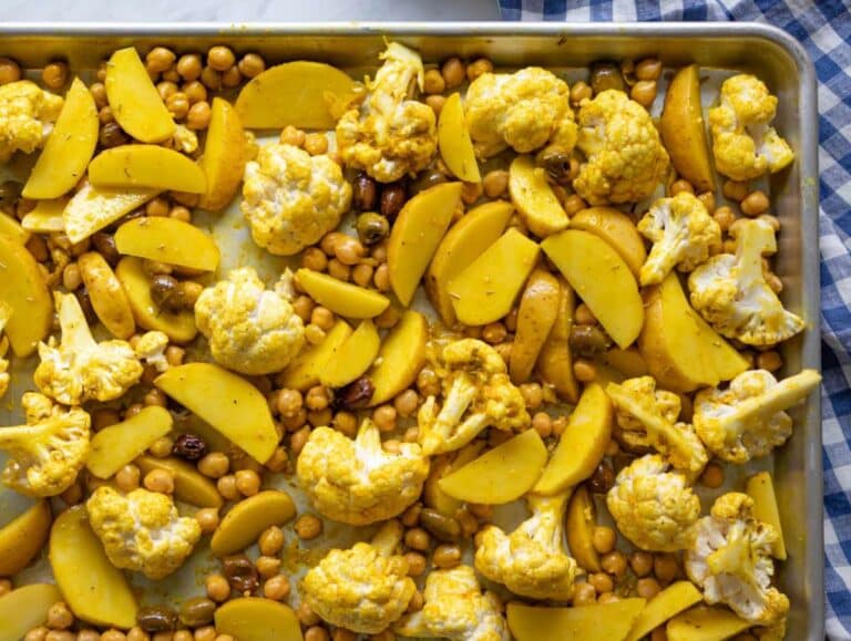 Step two tossing cauliflower potatoes chickpeas and olives with marinade on sheet pan.