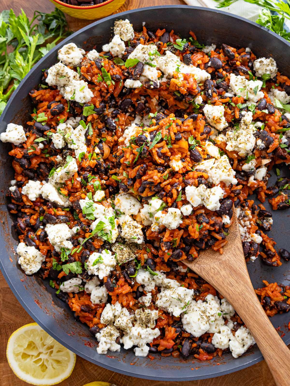 Top down view of black beans and rice in skillet topped with feta and lemon wedges.
