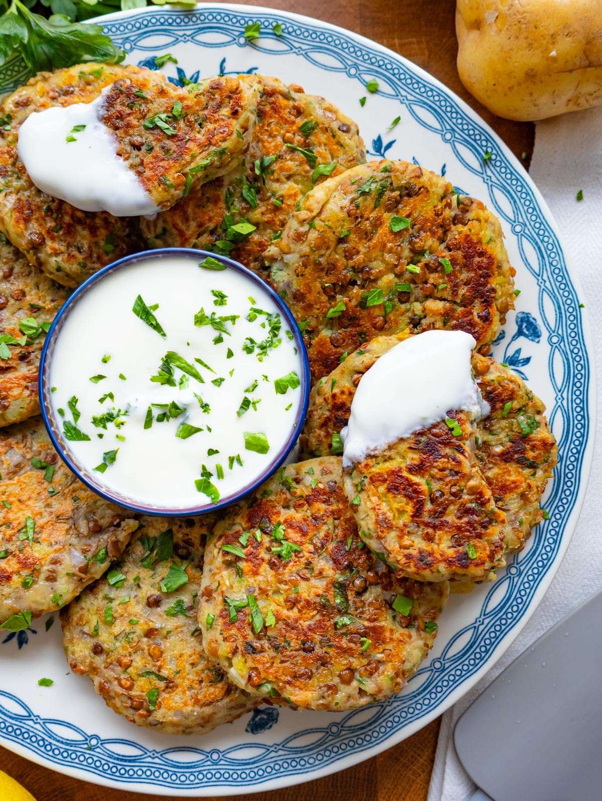 Top down view of golden lentil potato patties arranged neatly on a plate around a bowl of yogurt dip.