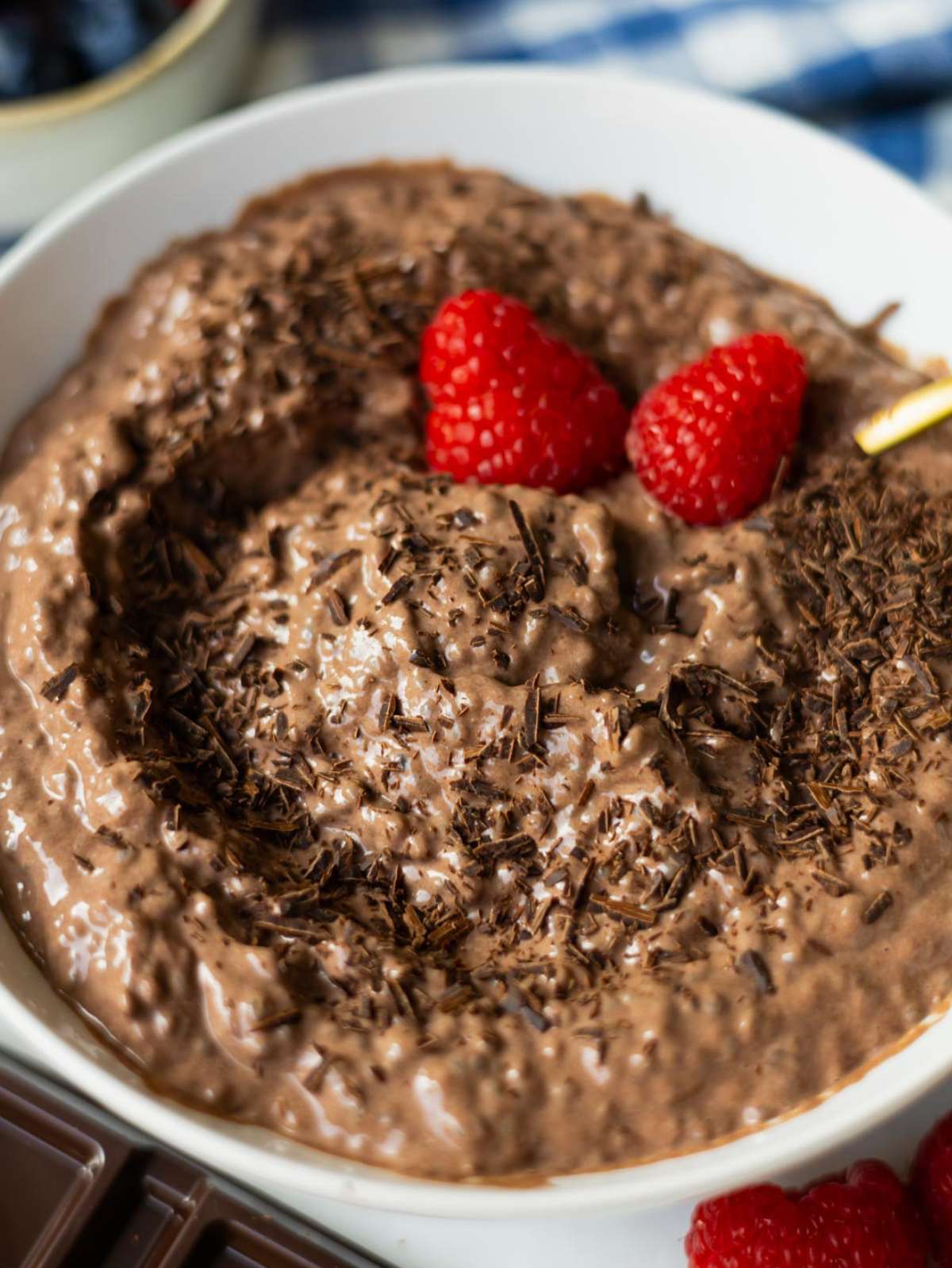 Chocolate chia pudding in a white bowl with shaved chocolate and berries on top.
