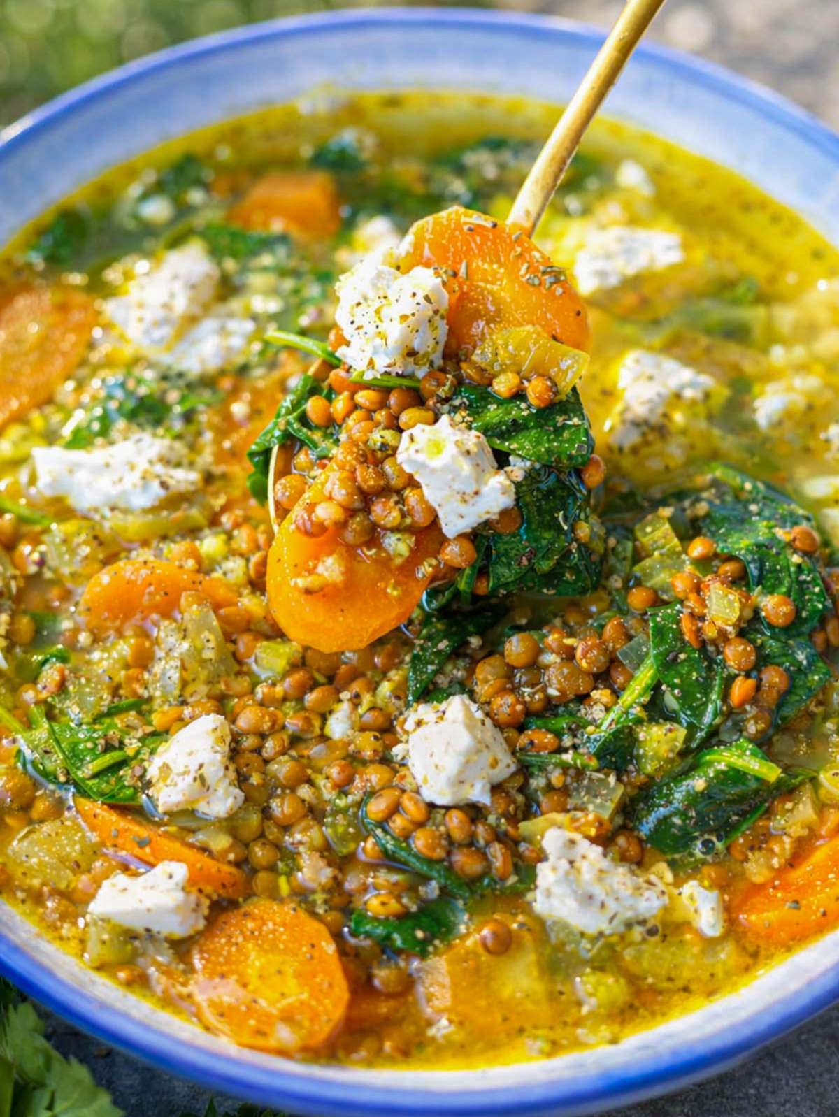 Close up lemon lentil soup showing lentils spinach and creamy feta topping.