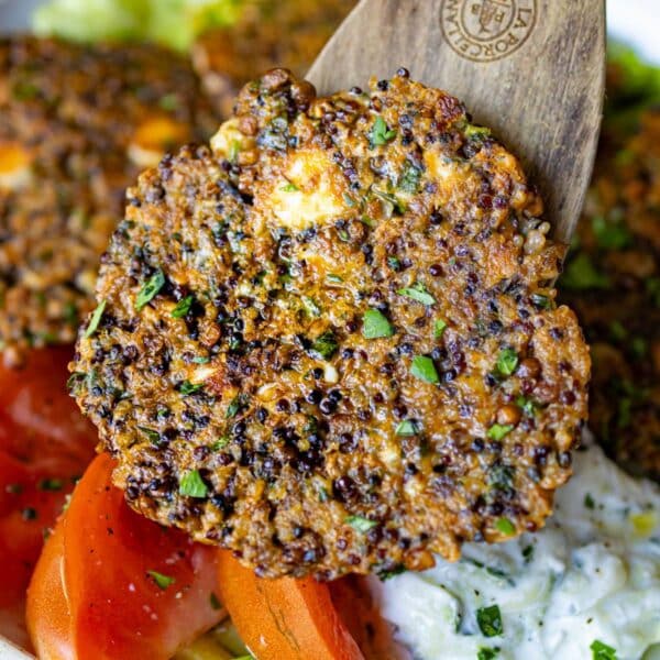 Close up of a lentil quinoa patty over a bowl with tomatoes tzatziki and lettuce.
