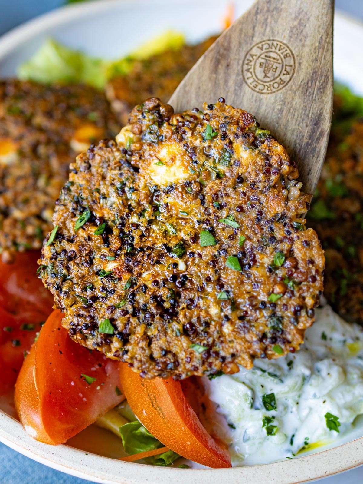 Close up of crispy lentil quinoa patties showing golden edges feta and fresh herbs.
