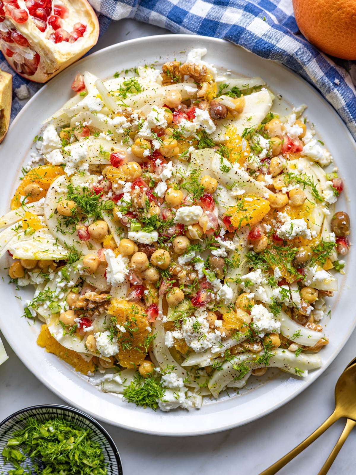 Finished orange fennel salad served on platter with olives walnuts and pomegranate.