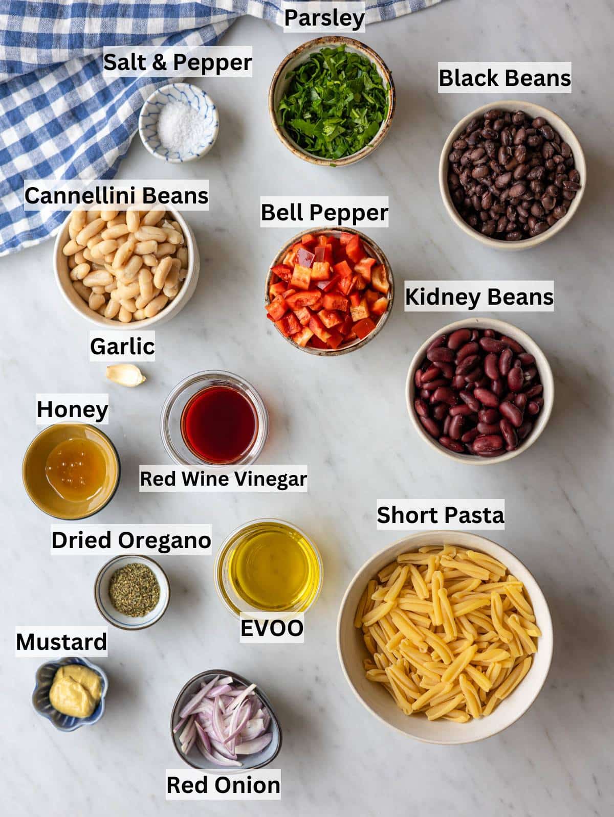 Ingredients for 3 bean pasta salad arranged on counter with beans pasta vegetables and dressing.