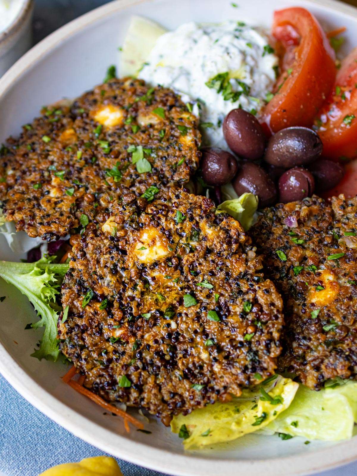 Lentil quinoa patties served in a bowl with lettuce tzatziki tomatoes and olives.