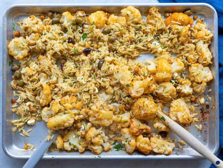 Step 3 Tossing hot orzo with roasted vegetables olives feta and parsley on sheet pan.