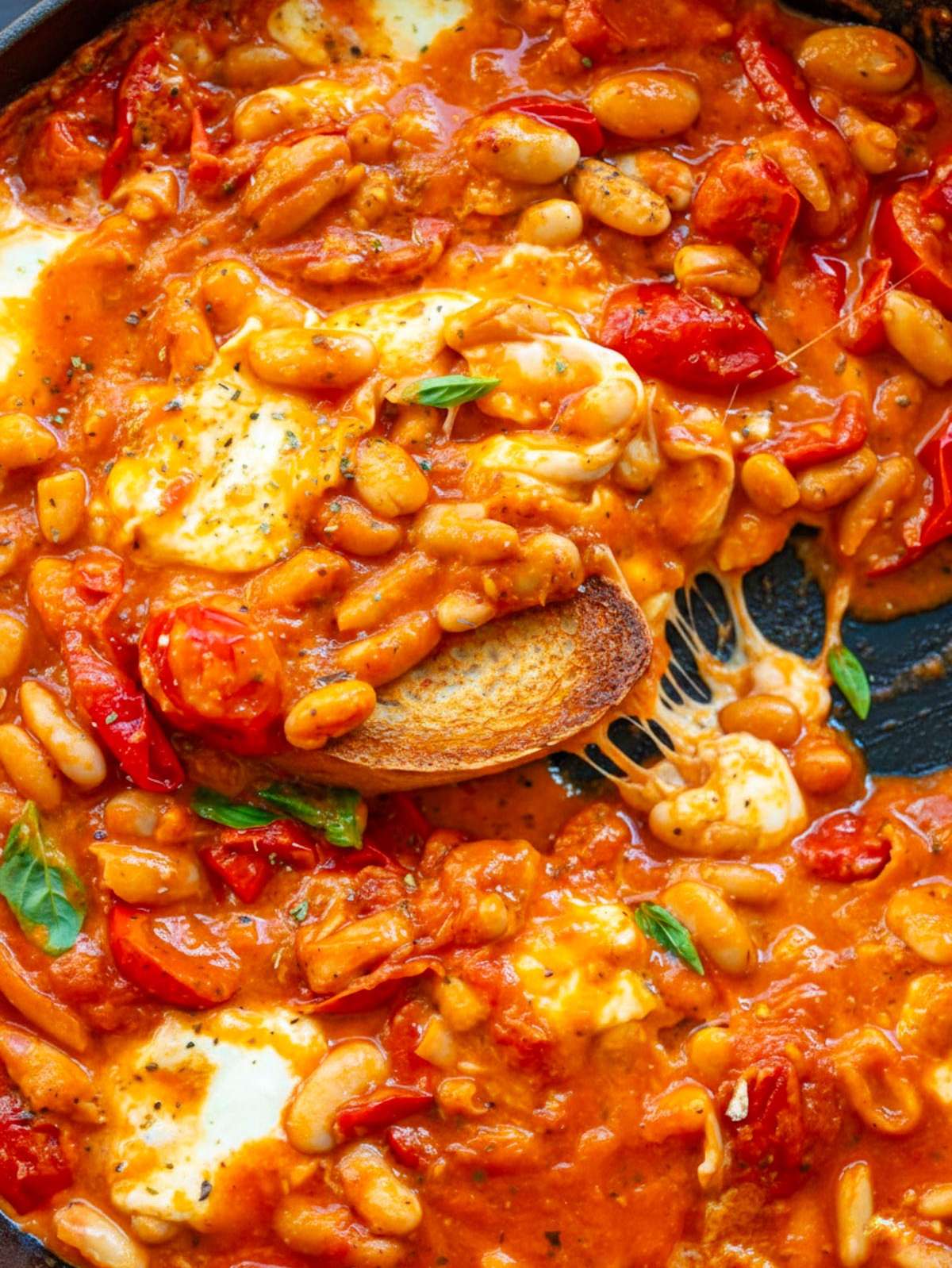 Top down view of pizza beans in skillet showing melted mozzarella and saucy beans.