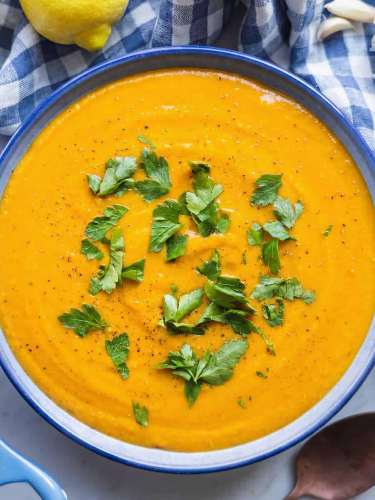 Top down view of sweet potato chickpea soup served in a bowl with herbs and black pepper.