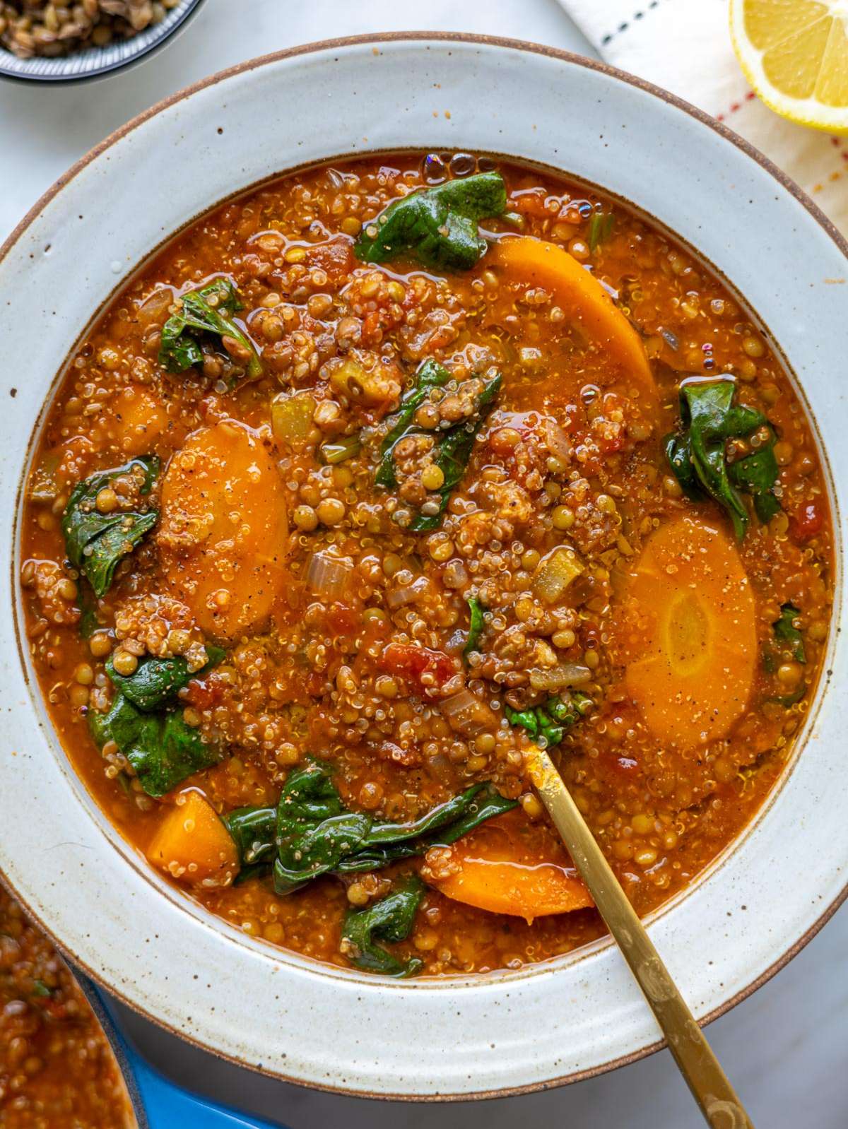 A warm bowl of quinoa vegetable soup ready to serve with lemon on the side.