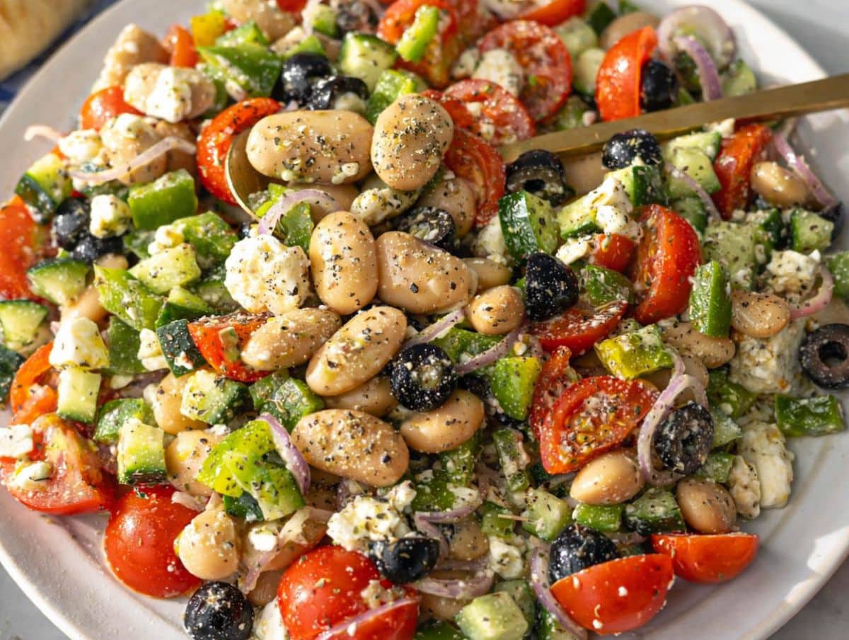 Bowl of Greek Bean Salad in natural light with rustic table setting and fresh ingredients.
