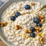 Bowl of Greek yogurt overnight oats topped with berries walnuts and honey.