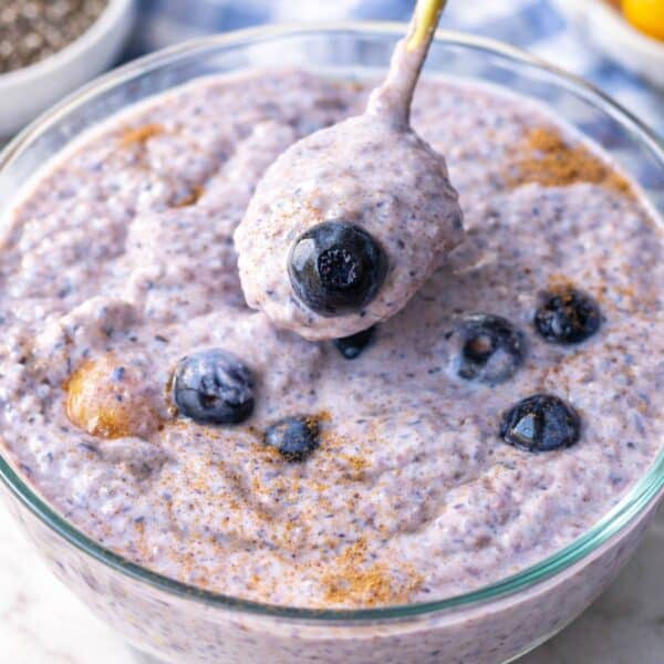 Bowl of blueberry chia pudding on a table with spoon and scattered blueberries in natural light.