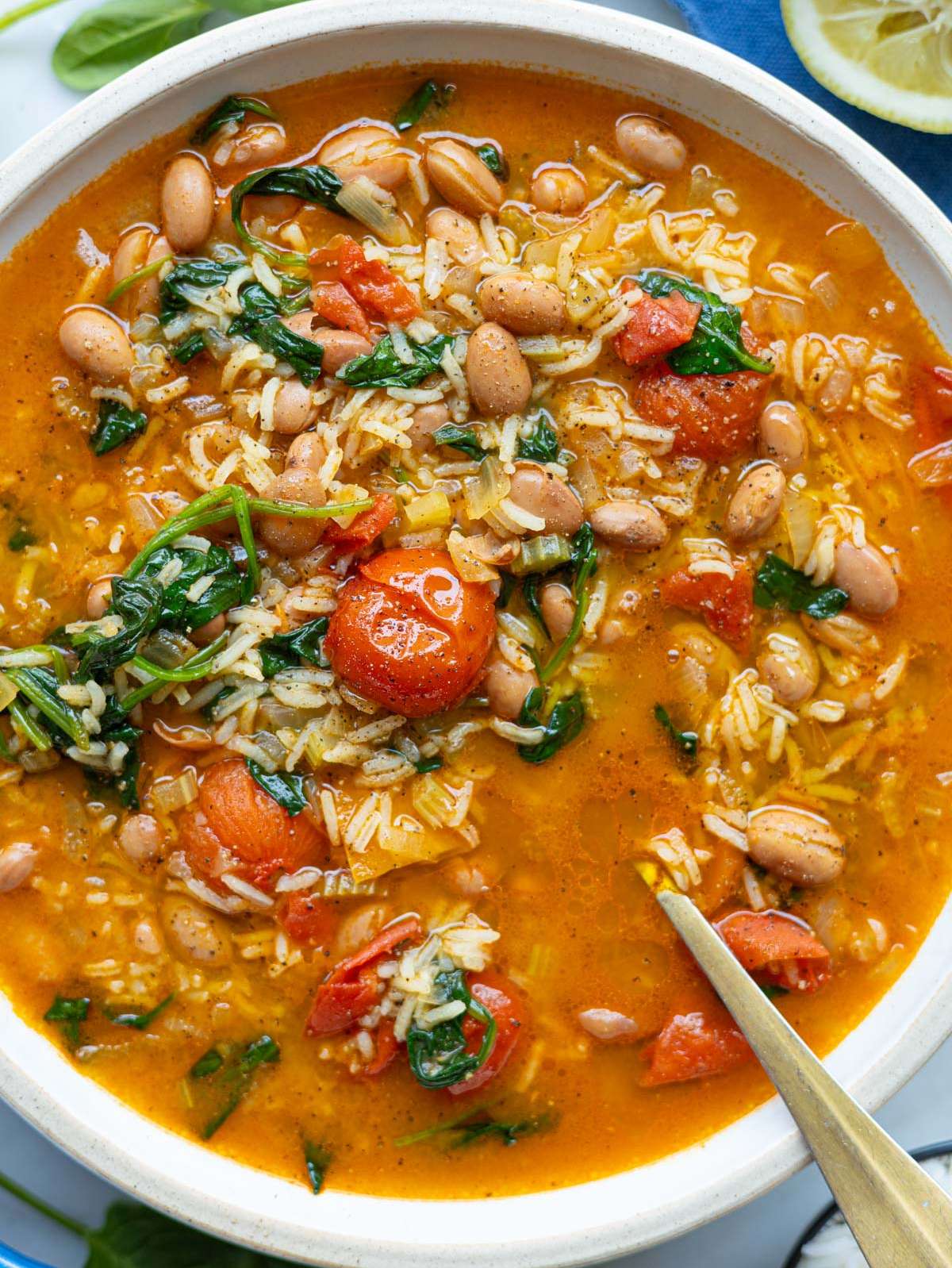 Bowl of pinto bean soup with burst cherry tomatoes, lemon juice, and olive oil.