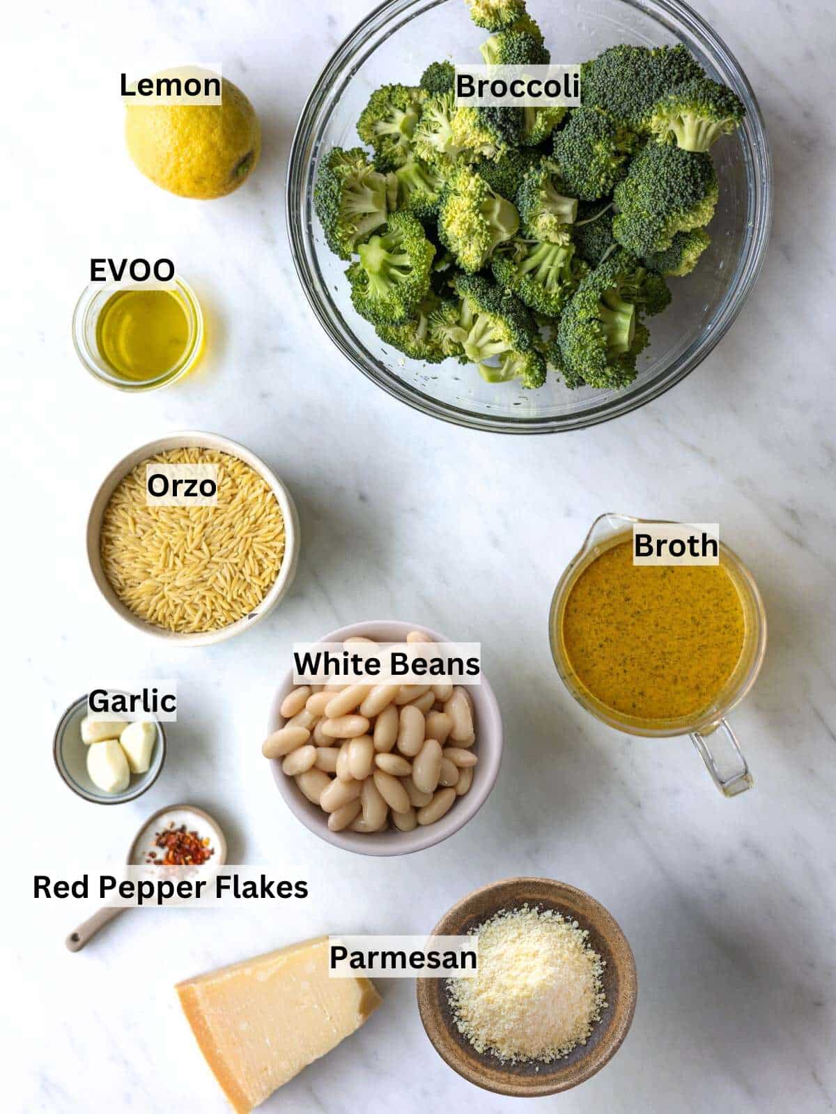 Broccoli florets, orzo, white beans, lemon, garlic, olive oil, and parmesan on a marble surface.