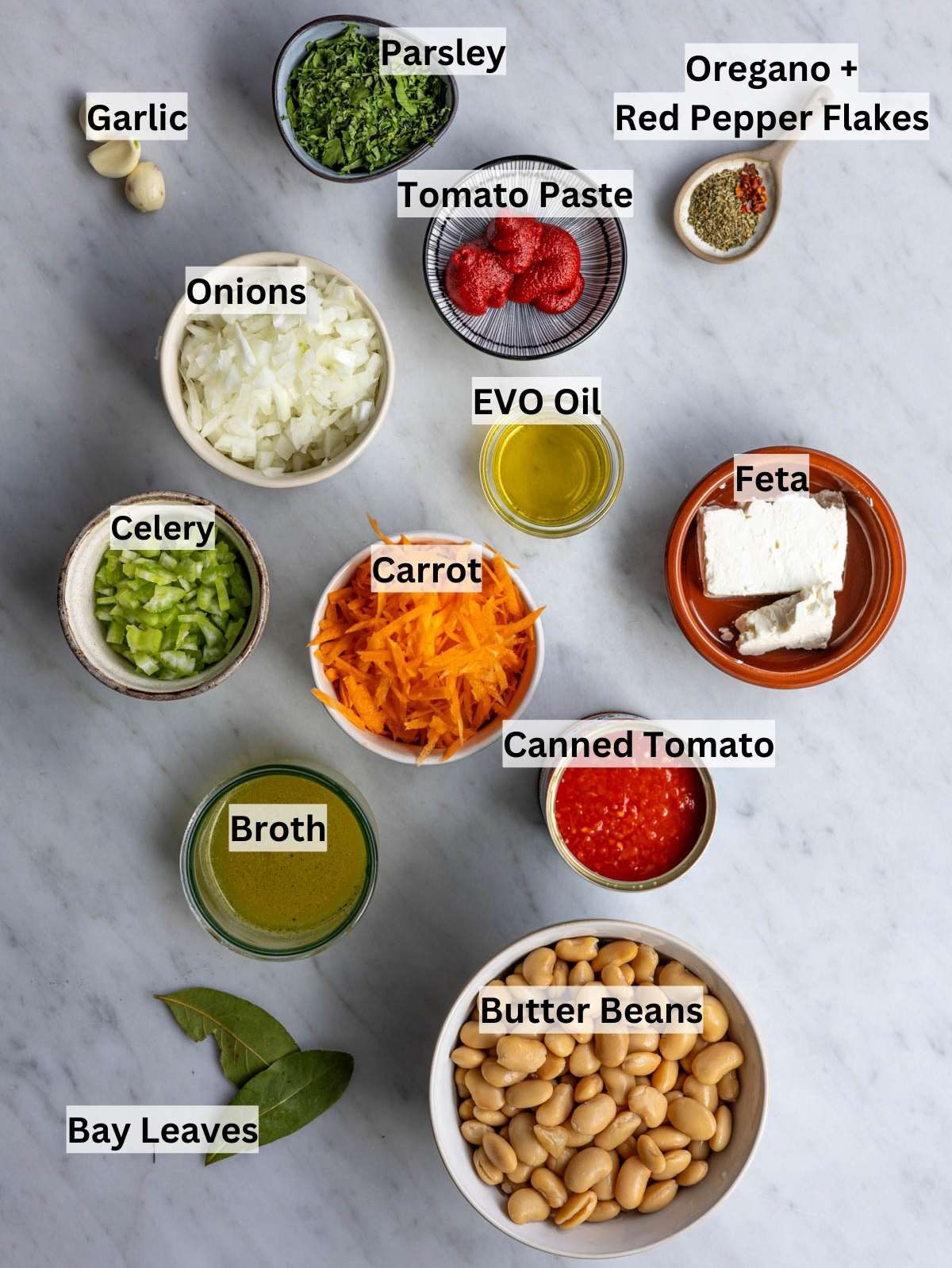 Butter beans tomatoes onion carrot celery garlic olive oil feta arranged on counter.