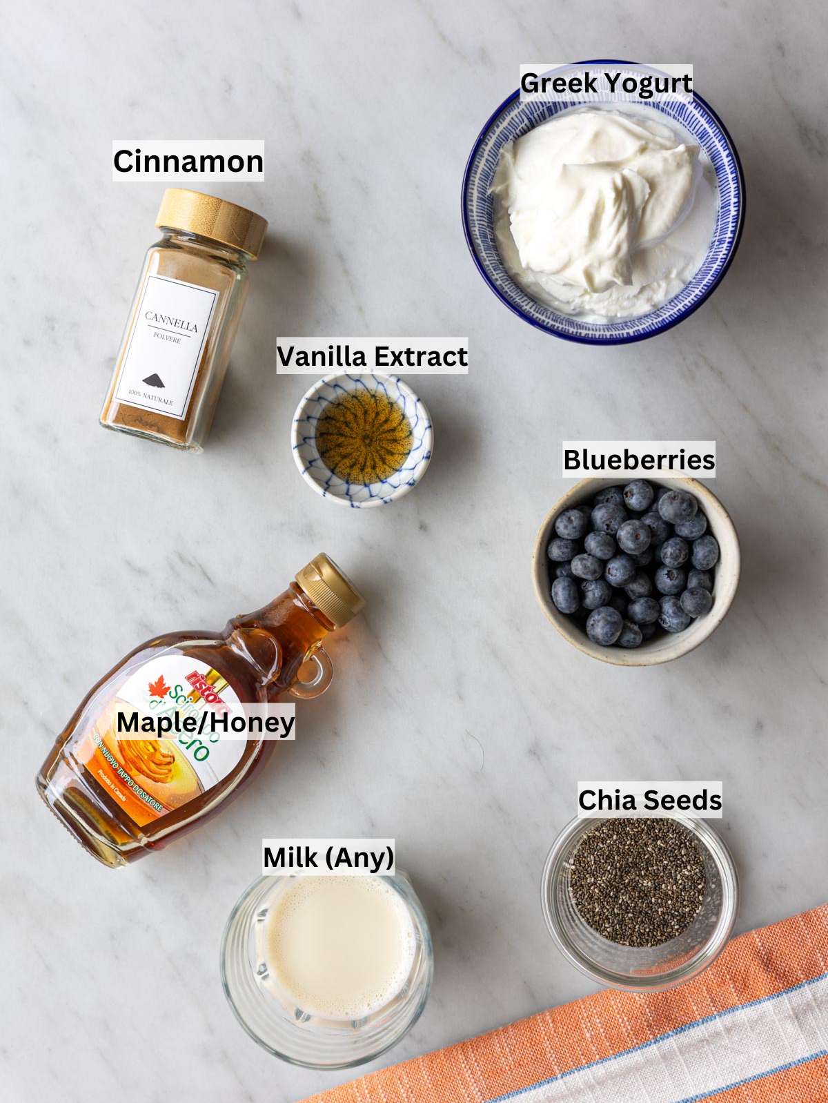 Chia seeds blueberries yogurt milk maple syrup cinnamon and vanilla arranged on a simple kitchen surface.
