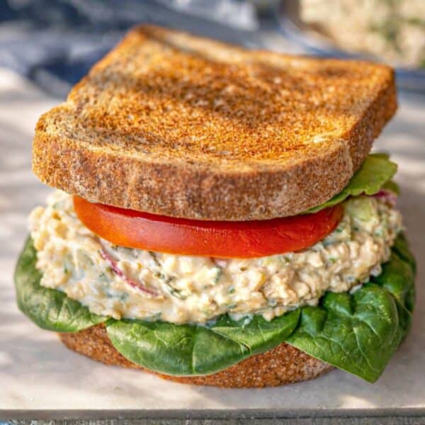 Chickpea Salad Sandwich with Greek Yogurt served on a marble cutting board with fresh vegetables.