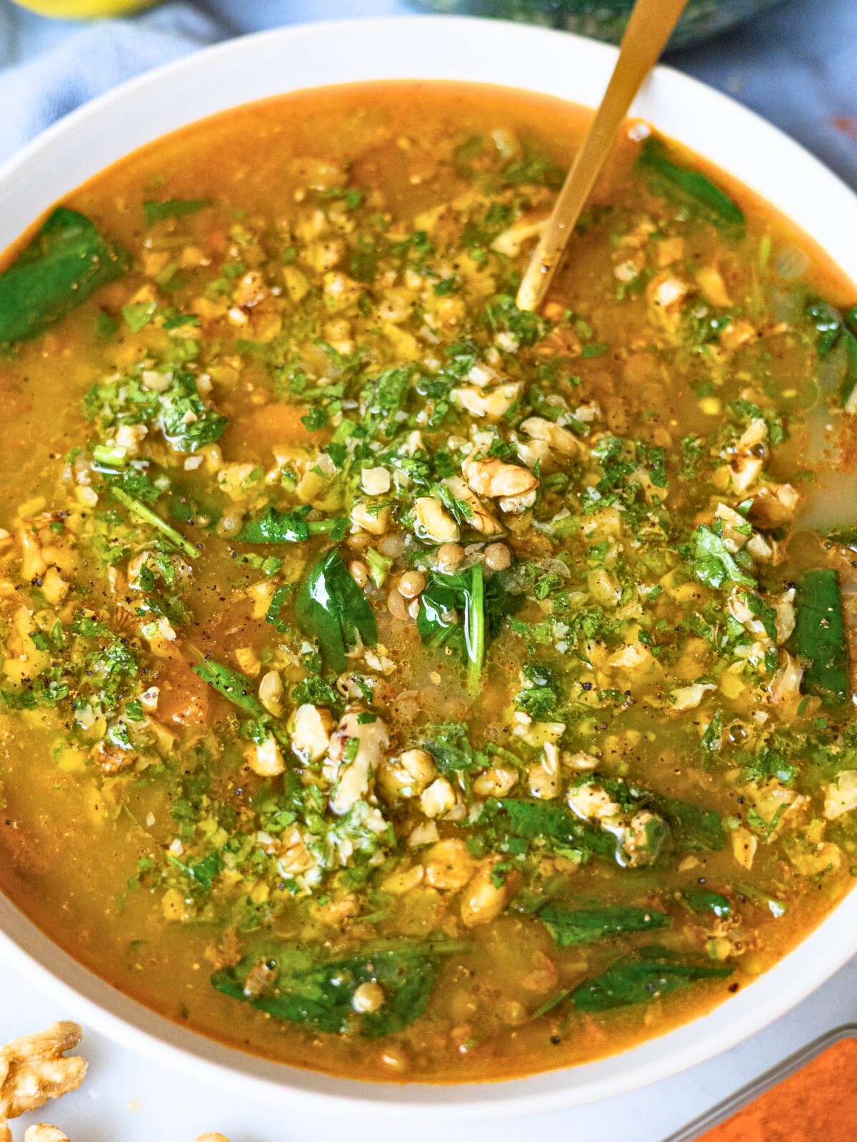 Close up of creamy lentil soup showing lentils spinach and crunchy walnut topping.