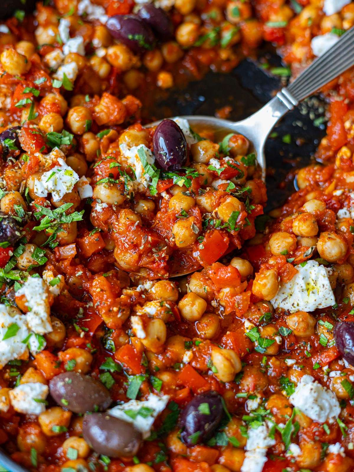 Close-up of thick chickpeas in rich tomato sauce with crumbled feta and olive oil.