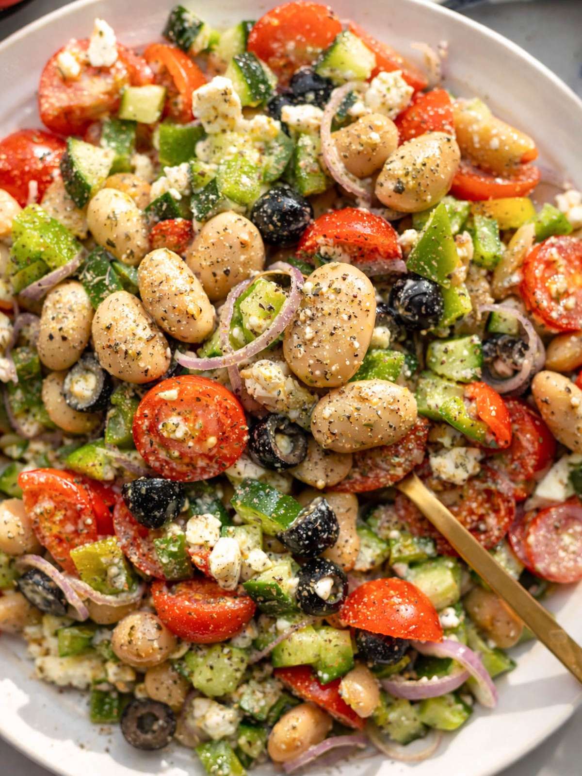 Greek Bean Salad served in a wide platter with feta, olives, and fresh vegetables.