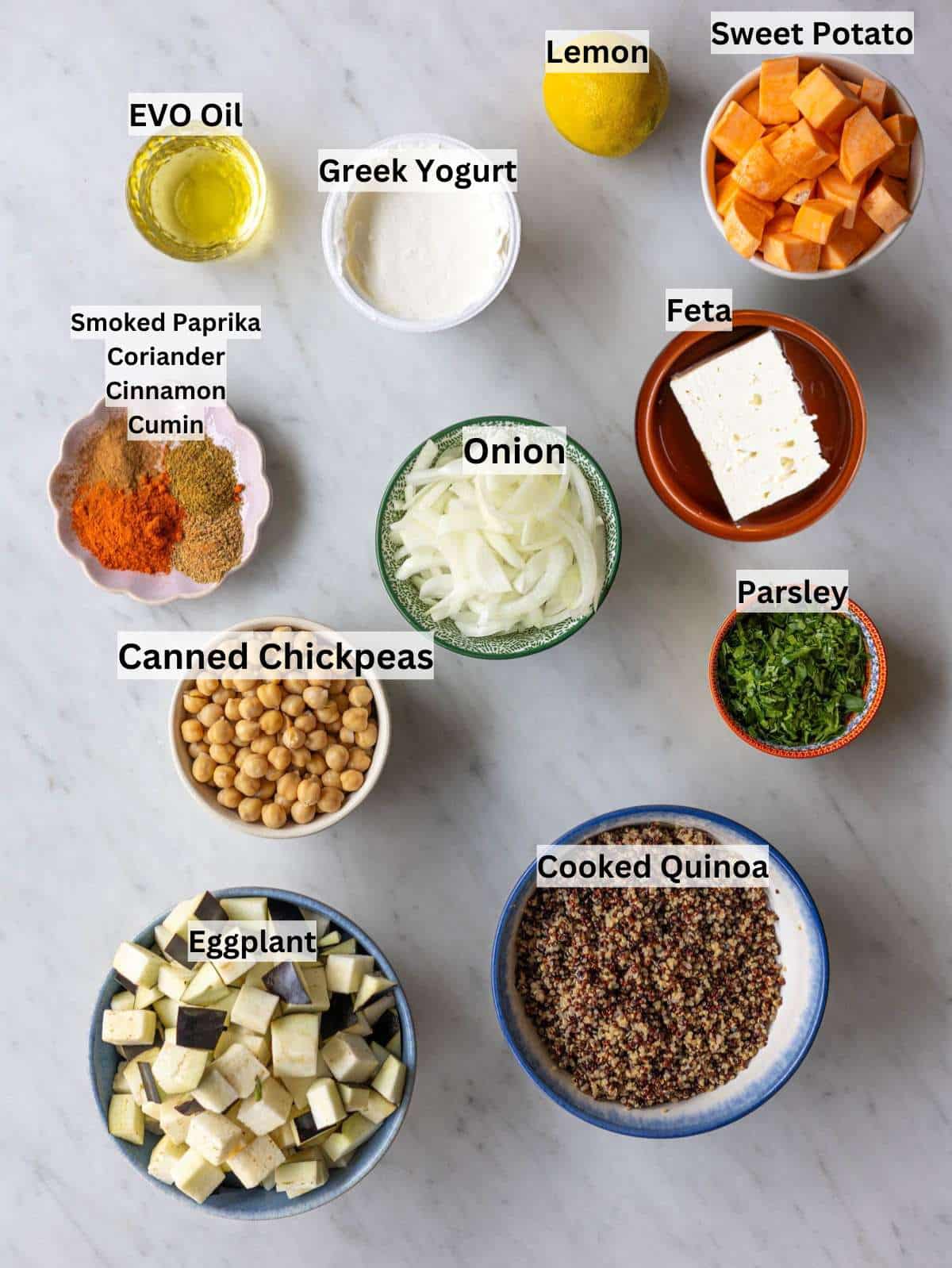 Ingredients arranged on a table with chickpeas, eggplant, sweet potato, spices, lemon, and olive oil.