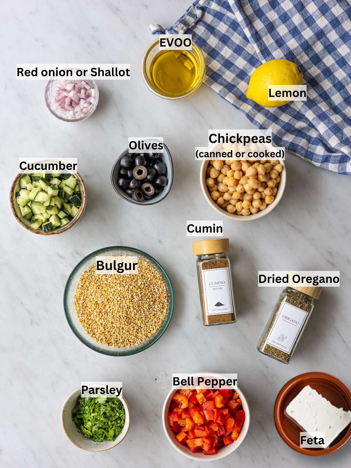 Ingredients for bulgur salad with chickpeas vegetables feta olive oil lemon and dried herbs arranged on table.