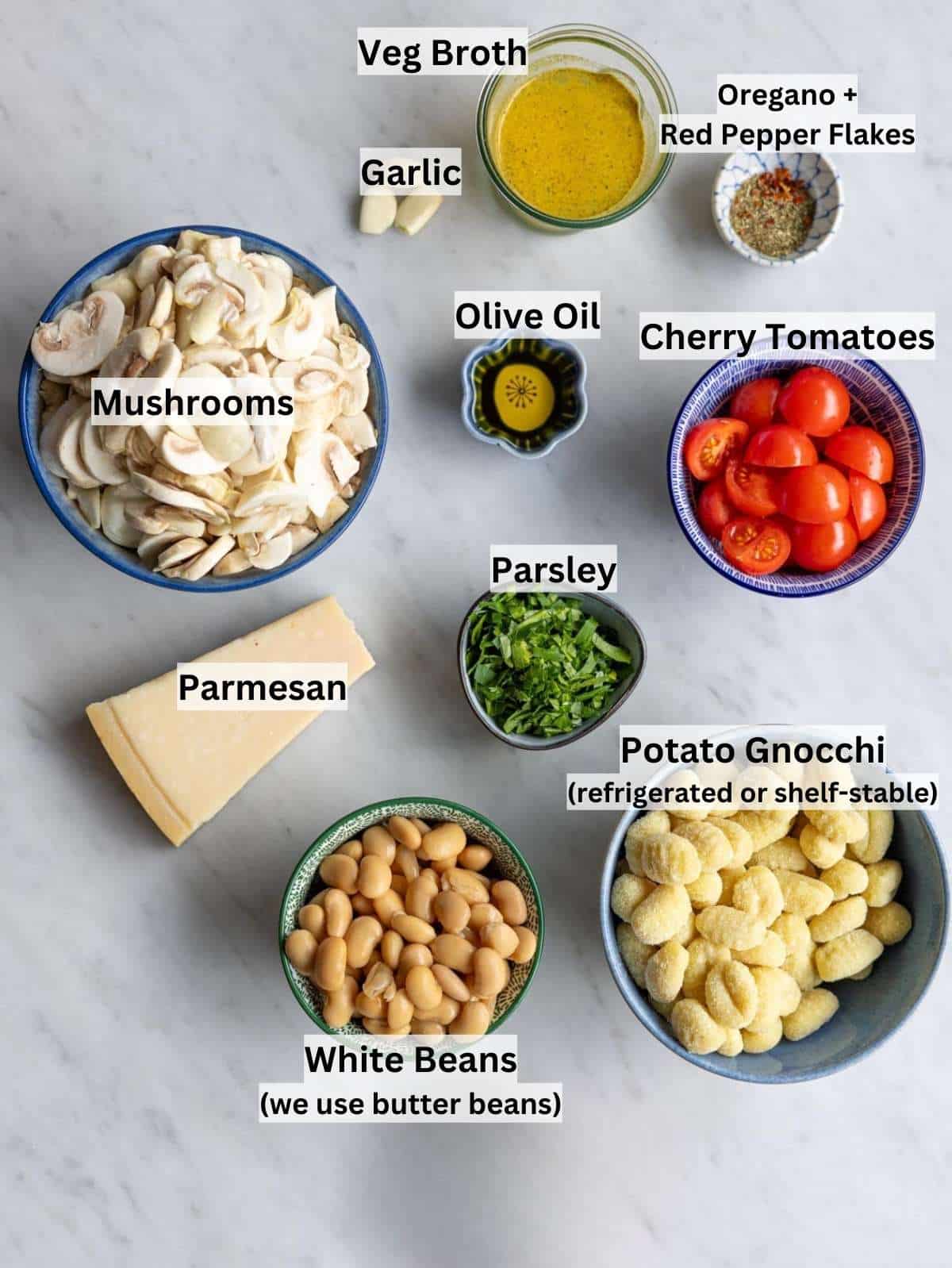 Ingredients for mushroom gnocchi laid out on a kitchen counter, including mushrooms, gnocchi, tomatoes, beans, and parmesan.