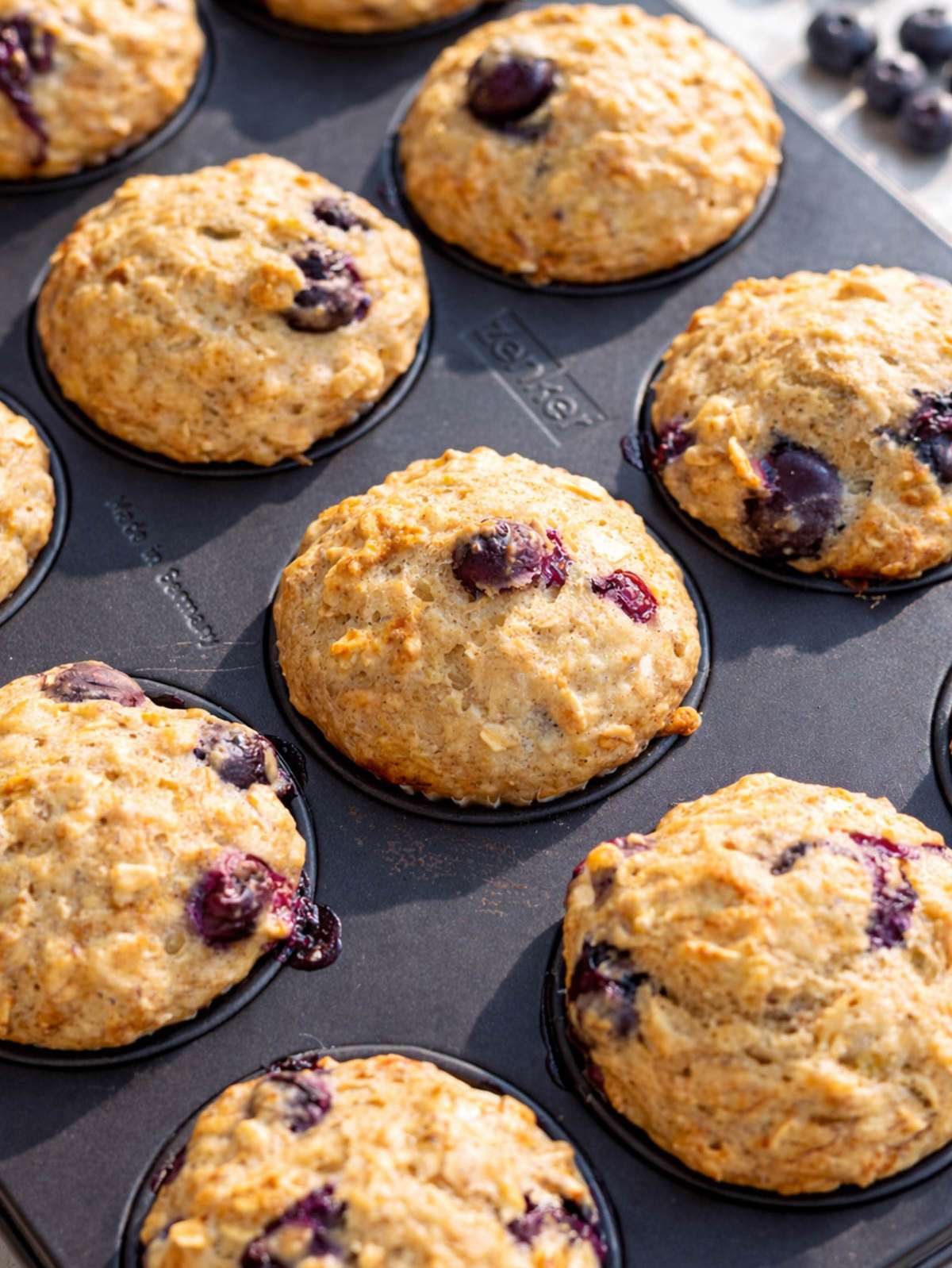 Just-baked blueberry muffins resting in the pan on a kitchen table in bright sunlight.