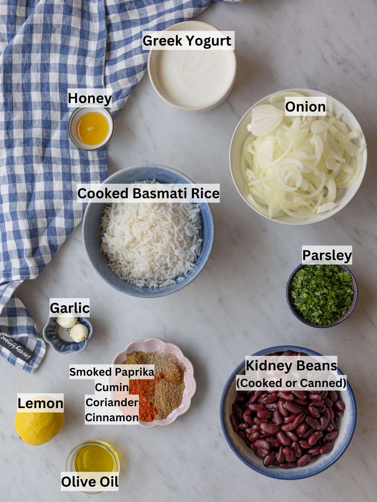 Kidney beans, cooked rice, onions, spices, lemon, parsley, olive oil, and yogurt arranged on a counter.