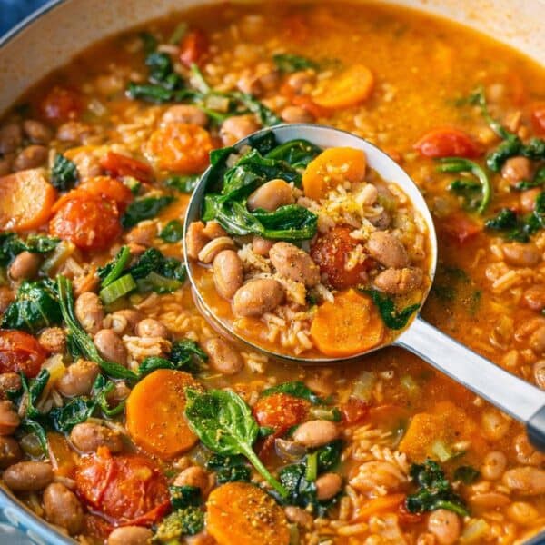 Ladle lifting pinto bean soup with beans, vegetables, and broth.