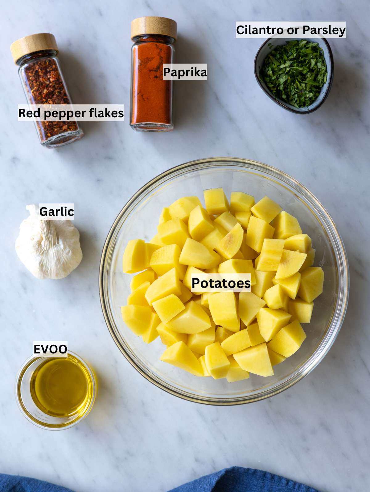 Raw potatoes garlic lemon olive oil spices and fresh herbs arranged on a simple kitchen counter.