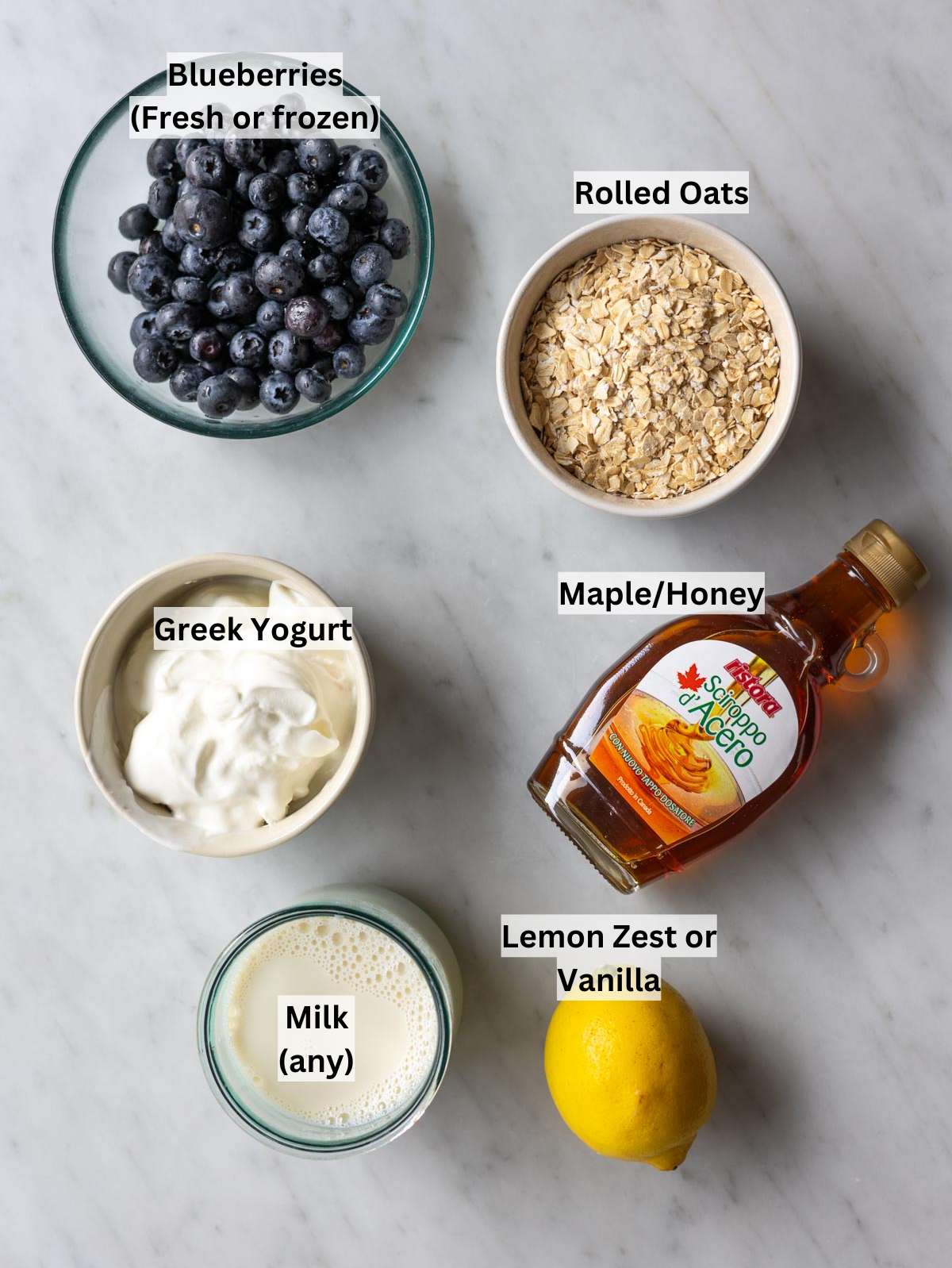 Rolled oats, blueberries, Greek yogurt, milk, maple syrup, and vanilla arranged on a kitchen counter.