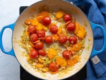 Step 1 Cherry tomatoes sizzling with onion, celery, and carrot in olive oil at the bottom of a large pot.