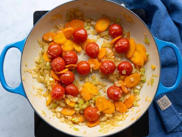 Step 1 Cherry tomatoes sizzling with onion, celery, and carrot in olive oil at the bottom of a large pot.