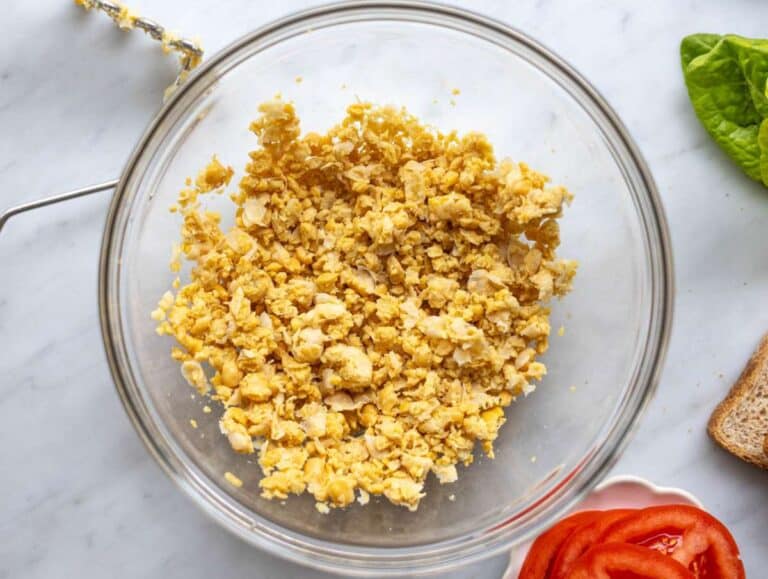 Step 1 Chickpeas mashed in a bowl with a potato masher, showing chunky texture before adding other ingredients.