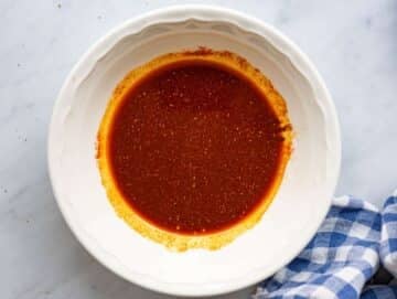 Step 1 Mixing bowl with olive oil, lemon juice, garlic, and spices being whisked together.